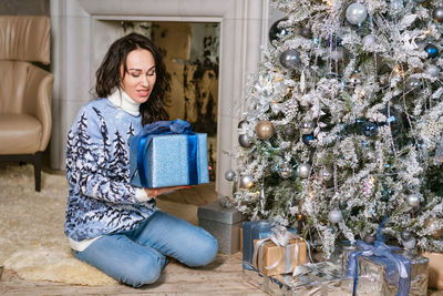 Beautiful woman in christmas sweater and jeans holds present or gift box