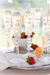 Five tall crystal flute glasses filled with sparkling rose wine, brightly lit from behind.