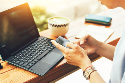 Close-up of female hands holding a mobile phone, in the background a laptop and a cup of tea 