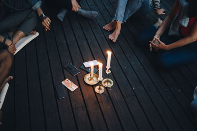 High angle view of friends sitting around lit candles and mobile phones in balcony during group therapy session