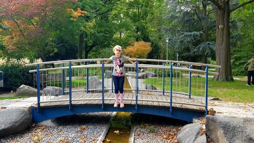 Portrait of smiling young woman standing on footbridge in park