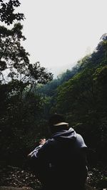 Rear view of man standing in forest against clear sky