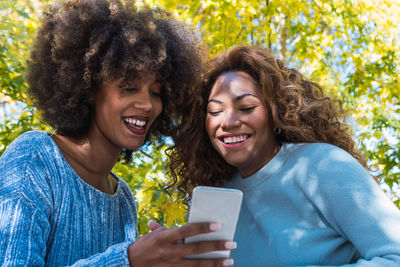 Two female afro american friends checking social media holding smartphone outdoors