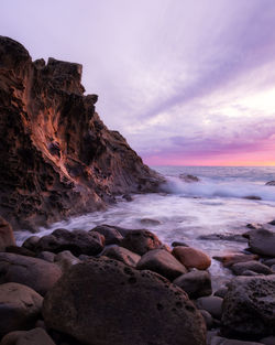 Rocks on beach against sky during sunset