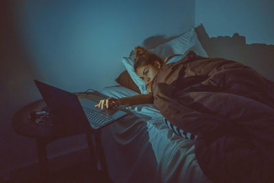 High angle view of woman using laptop while lying on bed at home