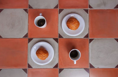 Two espresso cups - made from vietnamese coffee - and two plates of pain au chocolat on tiled floor