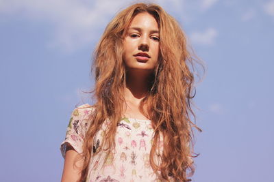 Low angle portrait of young woman with messy hair against sky