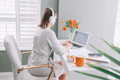 Rear view of woman working on laptop at home