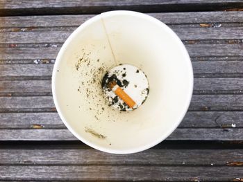 High angle view of burnt cigarette in disposable cup on wooden table