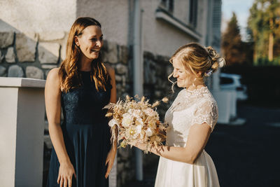 Bride holding bouquet while standing with friend during wedding ceremony