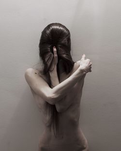 Topless mid adult woman with covered face standing against wall