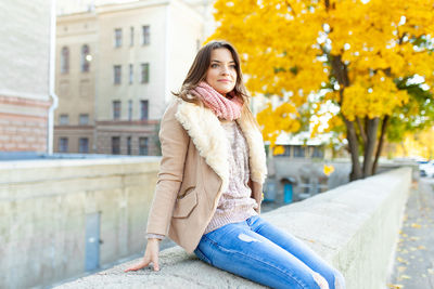 Young woman sitting on retaining wall during winter