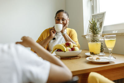 Smiling woman drinking coffee at dining table