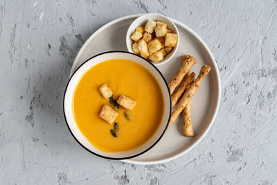 Top view of pumpkin, carrot cream soup in a bowl. with croutons, pumpkin seeds and bread sticks