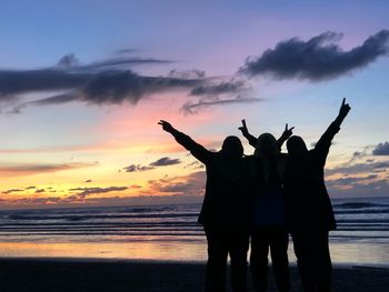 Silhouette people at beach against sky during sunset