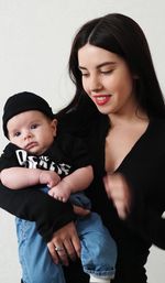 Portrait of young woman with little son standing against white background black clothes 