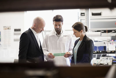 Engineer discussing machine with business people in factory