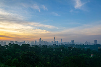 Trees and buildings against sky during sunset in city