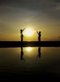 Silhouette man standing by lake against sky during sunset