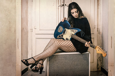 Full length of young woman playing guitar while sitting against doors