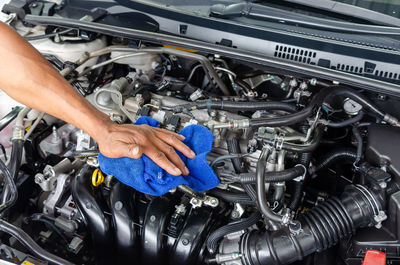 Cropped hand of man cleaning car engine with fabric