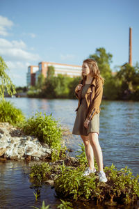 Side view of young woman standing by lake against sky