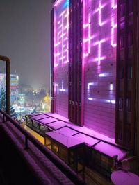 Illuminated street by buildings against sky at night in city