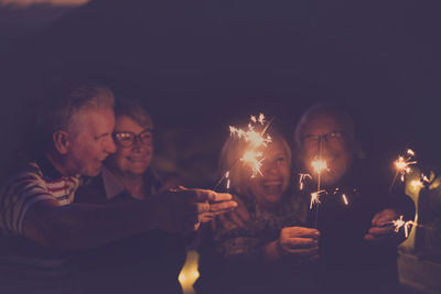 Happy senior couple playing with sparklers against sky at night