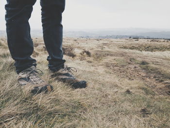 Low section of person standing on grass field against sky