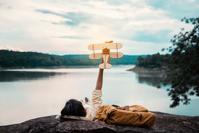 Rear view of woman standing on rock by lake against sky