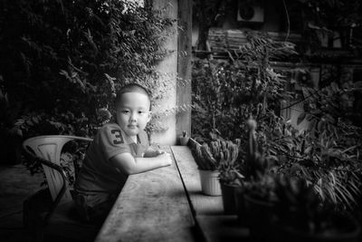Side view portrait of cute boy sitting by plants at backyard