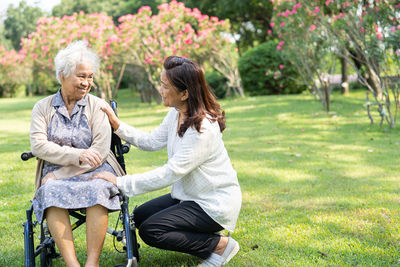 Caregiver help and care asian senior   woman patient sitting and happy on wheelchair in park,  