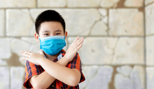 Portrait of boy wearing flu mask gesturing while standing against wall