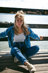 Young woman sitting on pier over sea against sky