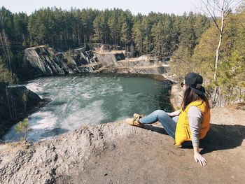 Rear view of woman sitting on rock against trees