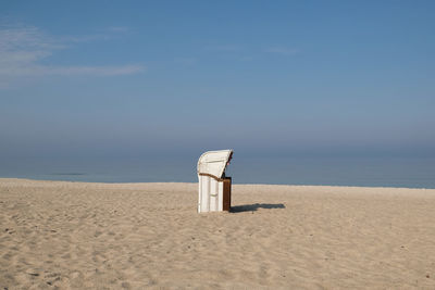 Hooded beach chair on sand against sky during sunny day