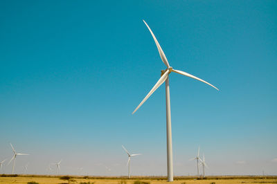 Low angle view of windmills against blue sky