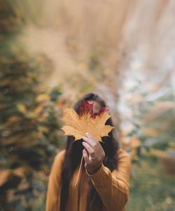 Close-up of woman holding maple leaf over face