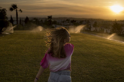 Rear view of woman standing on field against sky during sunset