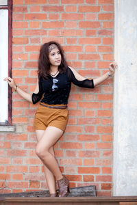 Fashionable young woman standing against brick wall