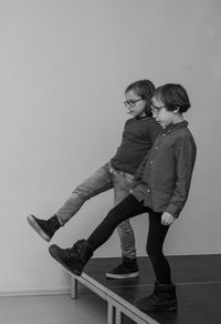 Full length of 2 boys, synchronously standing against wall