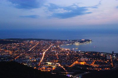 High angle view of illuminated city by sea against sky