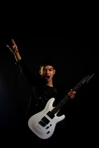 Young man playing guitar against black background