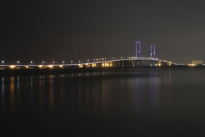 Illuminated bridge over river against sky at night