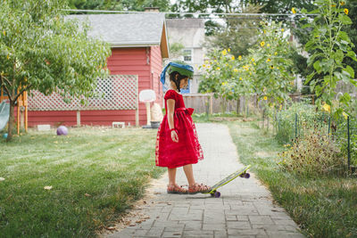 A girl in red dress and helmet steps on skateboard in garden in summer