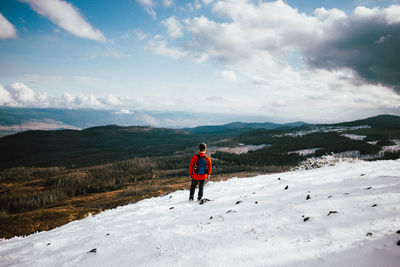 Rear view of man standing on snow against sky during winter