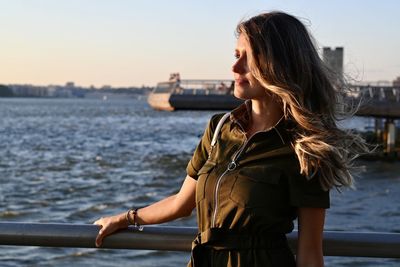 Side view of young woman standing by sea against sky during sunset