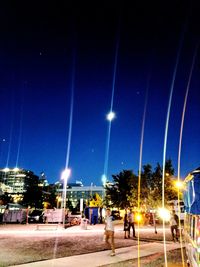 People in illuminated city against clear blue sky at night