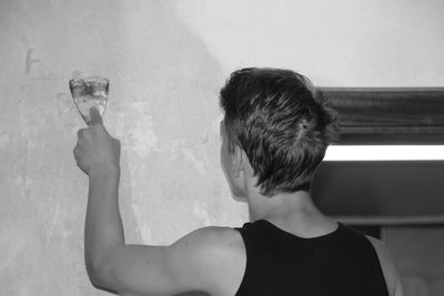 Rear view of young man plastering wall with scraper