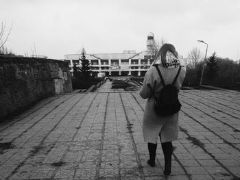 Woman walking towards building in city against sky